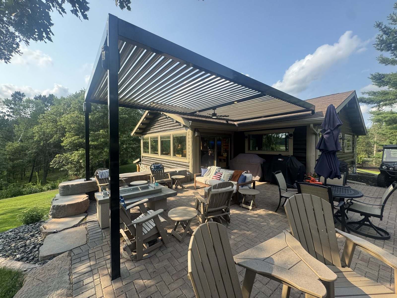 Black louvered pergola over a paver patio at a log cabin near the lake
